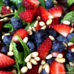spinach salad topped with strawberries, blueberries and pine nuts
