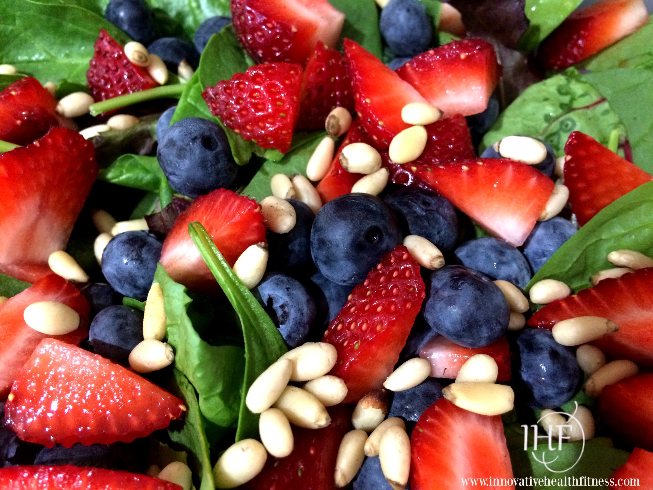 spinach salad topped with strawberries, blueberries and pine nuts
