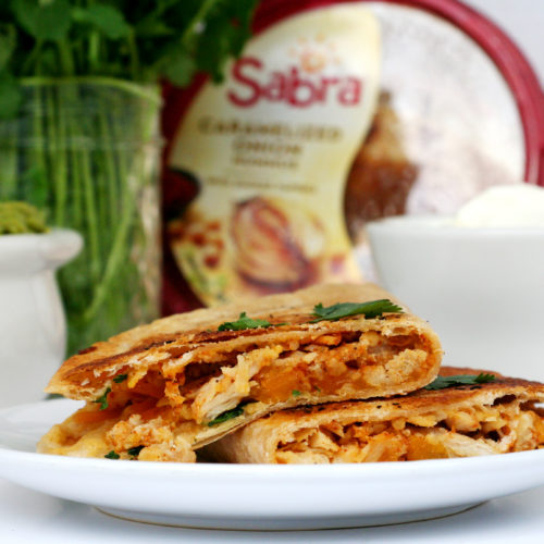 Sabra Hummus Chicken filled Quesadilla on white plate, cilantro, guacamole, sabra hummus and sour cream in the background.